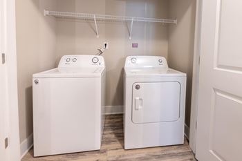 A white washing machine and dryer in a small laundry room at Foxwood Apartments, North Carolina, 27616